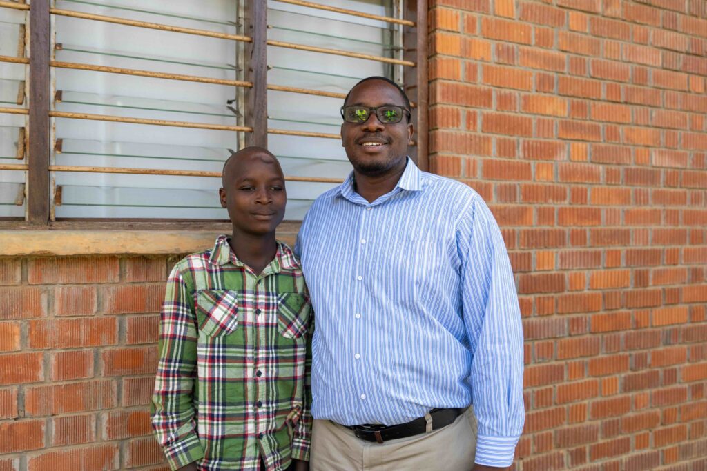 Dr. Emmanuel Wegoye, Neurosurgeon and Medical Director at CURE Uganda, stands with Isaac at CURE Uganda.